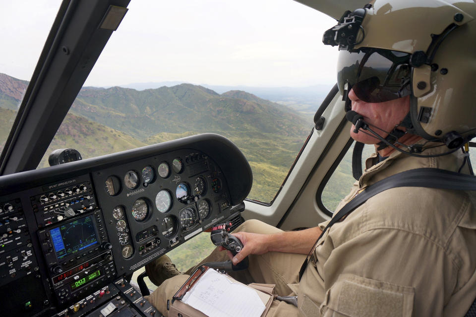 U.S. Customs and Border Patrol Air and Marine Operations Air Interdiction Agent Casey Russell searches above the Baboquivari Mountains, Thursday, Sept. 8, 2022, near Sasabe, Ariz. The desert region located in the Tucson sector just north of Mexico is one of the deadliest stretches along the international border with rugged desert mountains, uneven topography, washes and triple-digit temperatures in the summer months. Border Patrol agents performed 3,000 rescues in the sector in the past 12 months. (AP Photo/Giovanna Dell'Orto)