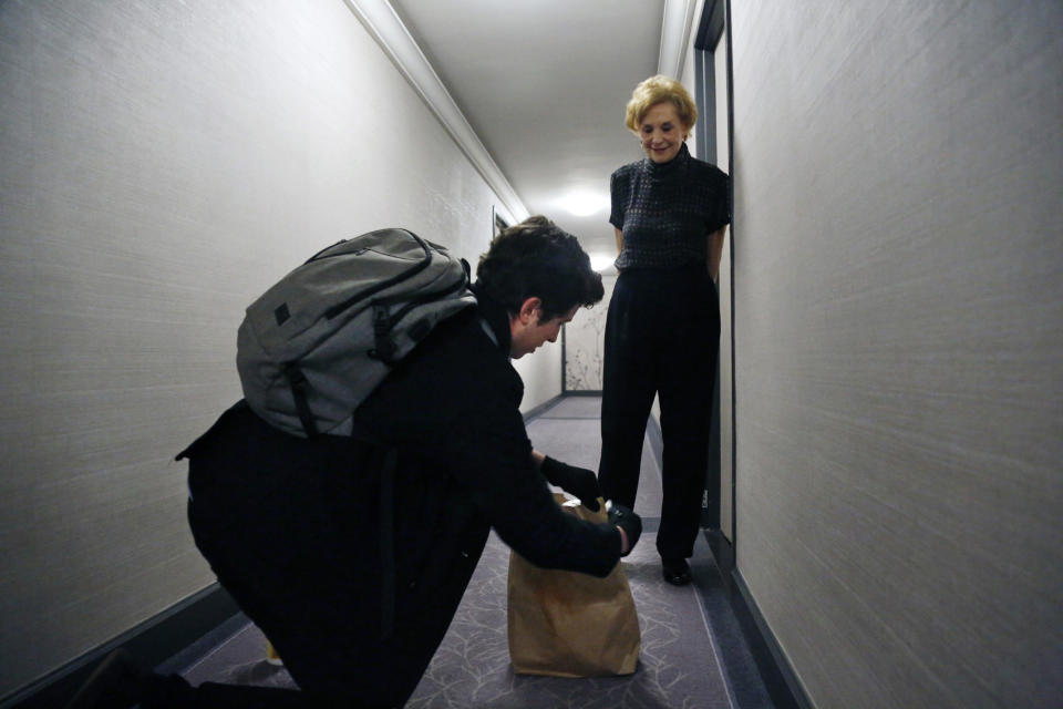 In this March 17, 2020, photo, Liam Elkind, 20, disinfects a paper bag full of groceries delivered to 83-year-old Carol Sterling, who is self-quarantined in her apartment in New York due to the coronavirus outbreak. Elkind continues to practice social distancing as he and Sterling make conversation in the hallway of her apartment. (AP Photo/Jessie Wardarski)