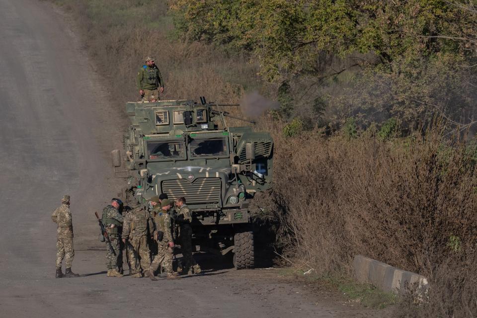 soldiers in camouflage near armored vehicle on dirt road