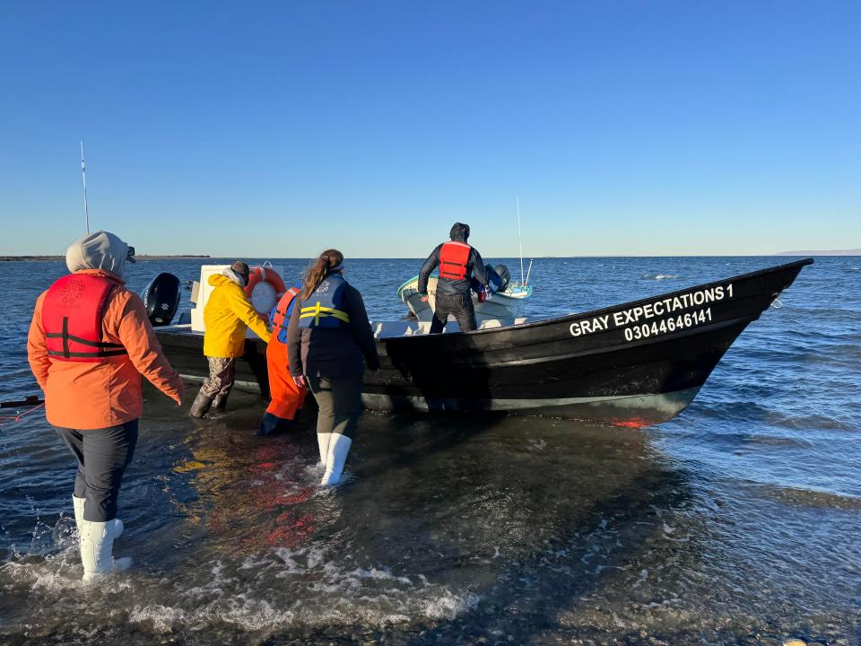 A group of people dressed in pants, boots, and jackets getting on a small boat called "Gray Expectations 1." 