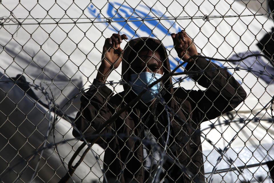 A migrant wearing a face mask stands behind a fence inside a refugee camp in Kokkinotrimithia outside of capital Nicosia, Cyprus, Friday, Feb. 5, 2021. Cyprus' Interior Minister Nicos Nouris said this week that the east Mediterranean island nation whose closest point to Syria is around 150 kilometers (93 miles) remains first among all other European Union member states with the most asylum applications relative to its population. Last year, the country of around 1.1 million people racked up 7,000 asylum applications - most of them from Syrians.(AP Photo/Petros Karadjias)