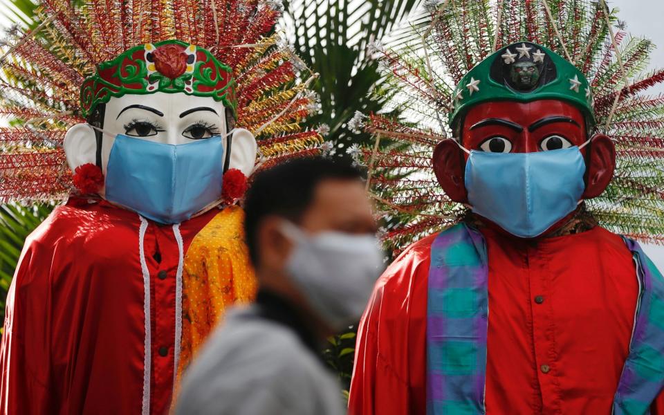 A man wearing a face covering walks past traditional Indonesian puppets – now also with masks – in Jakarta - Reuters