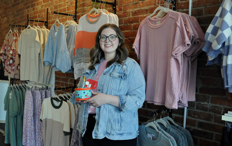 Opal and Olive's owner Alexys McQuillen stands by a rack of clothing. She is holding a dog toy, items that also are for sale. The store is named after her two dogs.