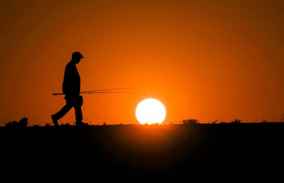 Nathaniel Robertson walks back to his car after fishing and braving the triple-digit warmth as the sun sets over Lake Pflugerville, Texas, on June 26, 2023.  Temperatures in Central Texas felt like 115+ degrees during the heat wave.