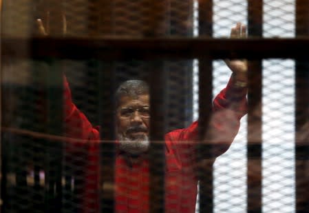FILE PHOTO: Egypt's deposed president Mohamed Mursi greets his lawyers and people from behind bars at a court wearing the red uniform of a prisoner sentenced to death, during his court appearance with Muslim Brotherhood members on the outskirts of Cairo