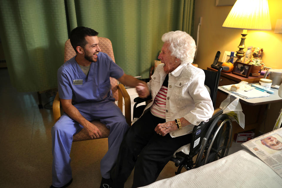 CHATHAM, MA - NOVEMBER 5: Nurses aid Nick Burrill shares a laugh with Broad Reach resident Laurie Hill, 101, in her room in Chatham, MA on Nov. 5, 2019. Struggling to find workers for his nursing home and assisted-living center in this seaside tourist town, Bill Bogdanovich tried a new strategy: buying properties on the southeastern elbow of Cape Cod to rent to employees like Burrill. He offered below-market rents to workers, many recruited from off the Cape and as far away as Puerto Rico, who were having trouble finding places to live. A year later, his gambit appears to have paid off: Bogdanovich has been able to hire and retain more workers - the better for his senior housing residents, and for business. (Photo by John Tlumacki/The Boston Globe via Getty Images)