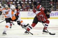 New Jersey Devils defenseman Ryan Graves (33) skates with the puck as he is checked by Philadelphia Flyers center Claude Giroux (28) during the first period of an NHL hockey game Sunday, Nov. 28, 2021, in Newark, N.J. (AP Photo/Bill Kostroun)