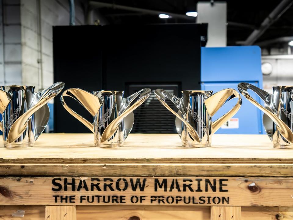 four shiny steel propellers with loops for blades lined up on a wood table with words painted on it: "sharrow marine the future of propulsion"