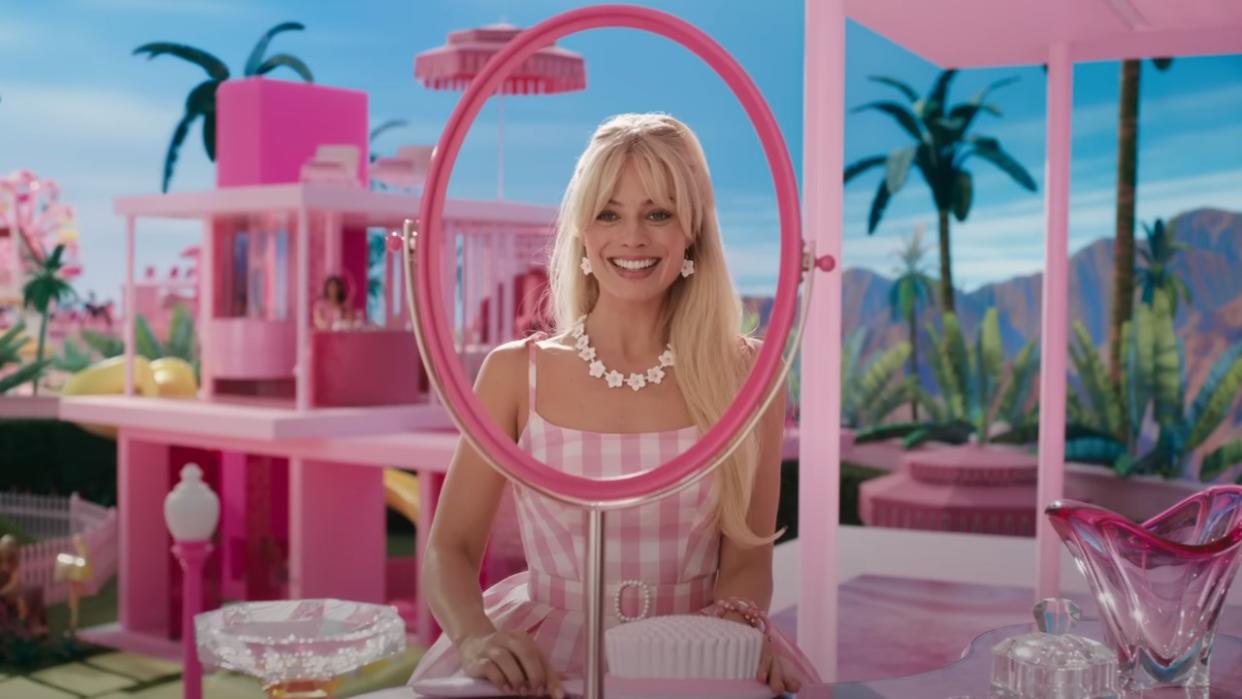  Margot Robbie as Barbie looking into a bright pink mirror. 