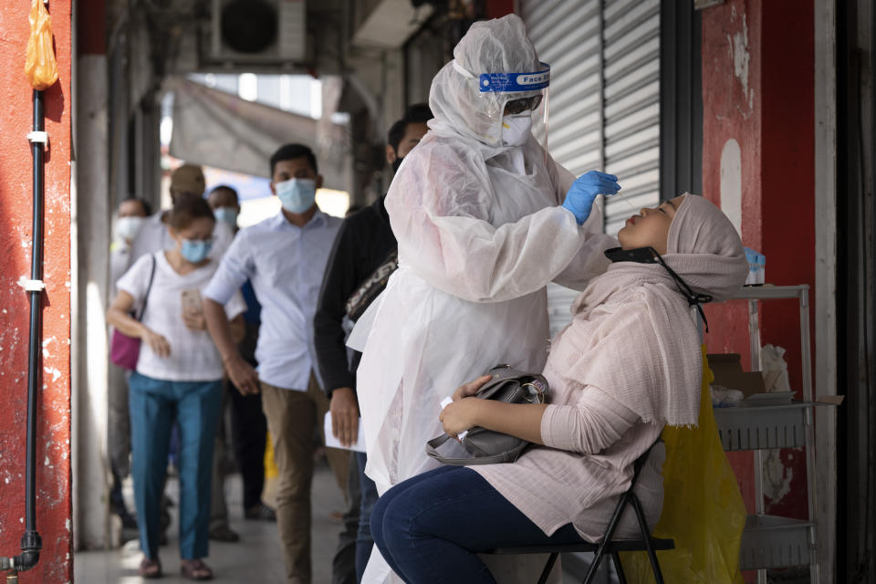 A doctor collects a sample for a coronavirus test outside a clinic in Kajang on the outskirts of Kuala Lumpur, Malaysia, Friday, Oct. 23, 2020. Malaysia restricted movements in its biggest city Kuala Lumpur, neighbouring Selangor state and the administrative capital of Putrajaya from Wednesday in an attempt to curb a sharp rise in coronavirus cases. (AP Photo/Vincent Thian)