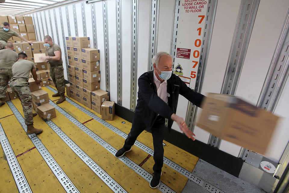 In this Sunday, April 12, 2020 photo, Arkansas Gov. Asa Hutchinson, right, helps Arkansas National Guardsmen unload a truckload of personal protective equipment at the Federal Surplus Warehouse in Little Rock, Ark. (Tommy Metthe/The Arkansas Democrat-Gazette via AP)