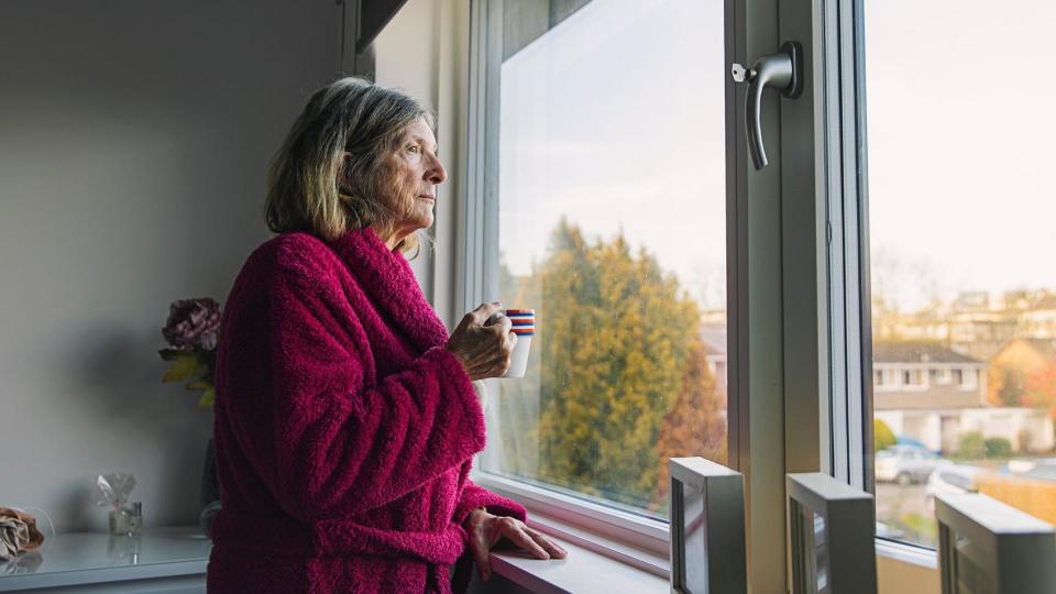 Una mujer mayor mira por una ventana. 