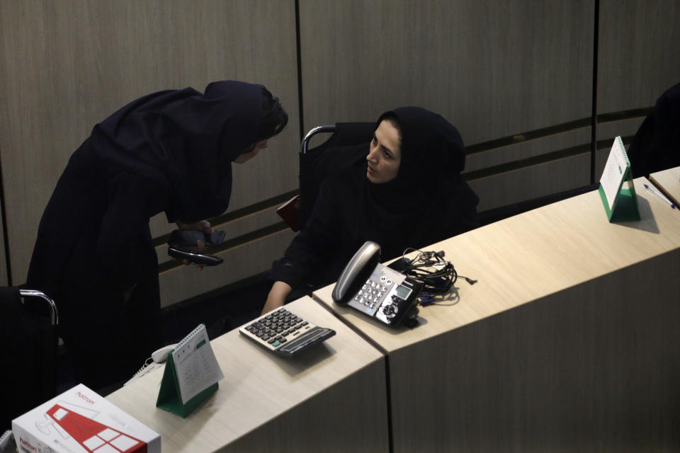 In this Sunday, May 10, 2020 photo, two stockbrokers talk at the Tehran Stock Exchange in Iran. The exchange has seen gains of 225% in the last year, with sharp increases even as the country struggled with one of the first serious coronavirus outbreaks outside of China. Encouraged by a government eager to privatize state-owned firms, average people now have access to the market and can trade shares. (AP Photo/Vahid Salemi)