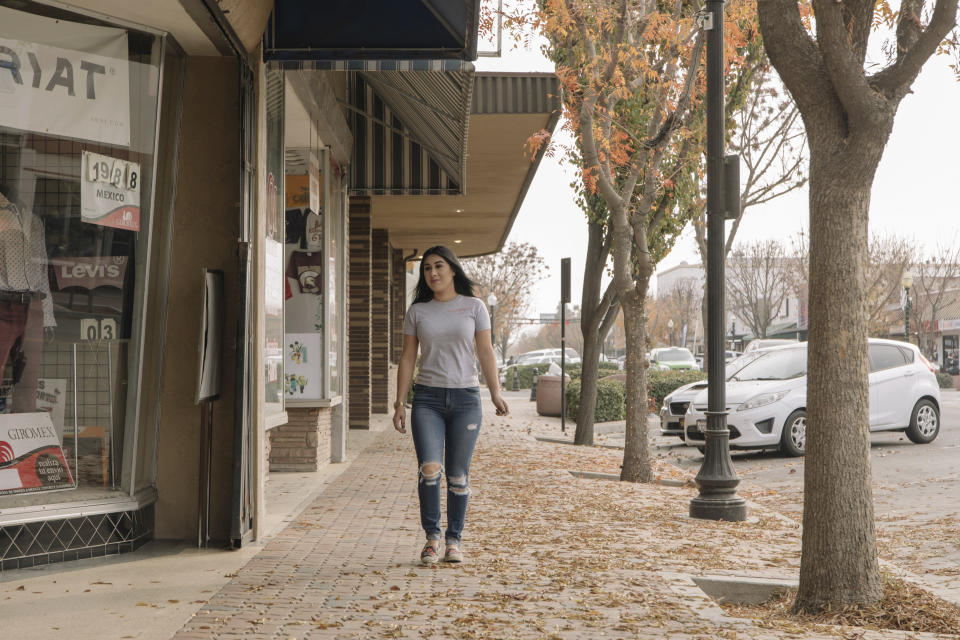 Alexandra Orozco walks down the main street of Delano, Calif., on Sunday, Dec. 6, 2020. Just over a two-hour drive from Los Angeles, the population of Delano is roughly 50,000, and jobs are scarce, she says. (Madeline Tolle/The Fuller Project via AP)