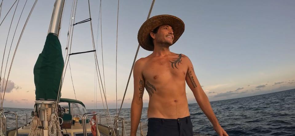 A man wearing a hat standing on a boat in the middle of the ocean.