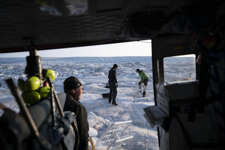 In this Aug. 16, 2019, photo, New York University air and ocean scientist David Holland, left, and field safety officer Brian Rougeux, right, are helped by pilot Martin Norregaard as they carry antennas out of a helicopter to be installed at the Helheim glacier, in Greenland. Holland and his NYU team are tracking what's happening in Greenland from both above and below. He calls it "the end of the planet" referring to geography more than the future. Yet in many ways Greenland is where the planet's warmer and watery future is being written. (AP Photo/Felipe Dana)