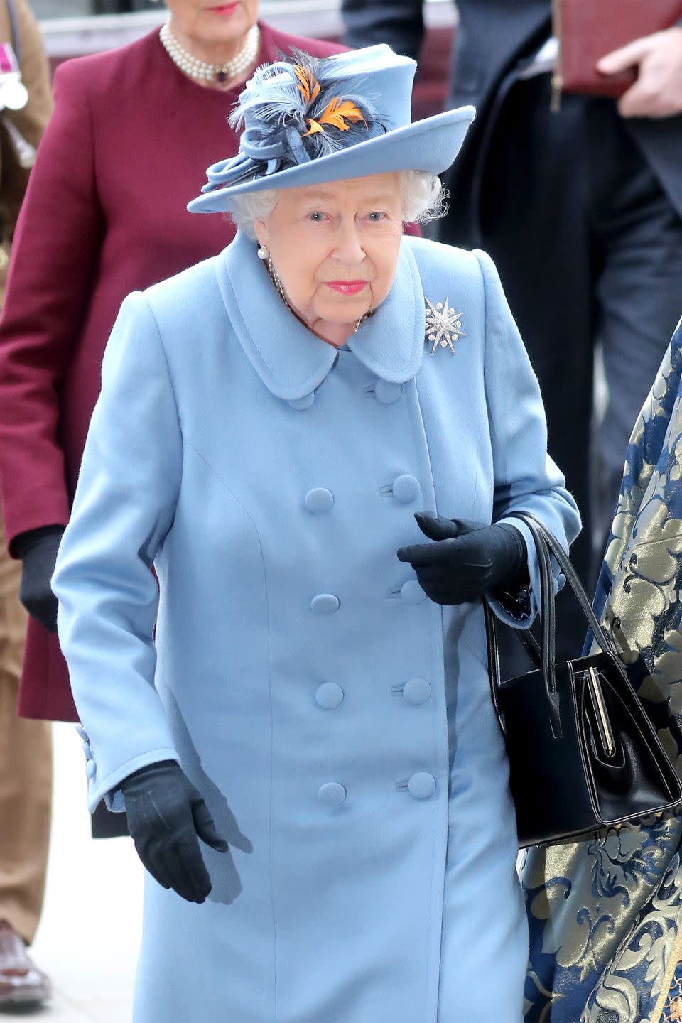 <p>Her Royal Majesty's dusted-blue outfit includes a pale periwinkle coat and matching hat, a broach, a black handbag, and navy gloves.</p>