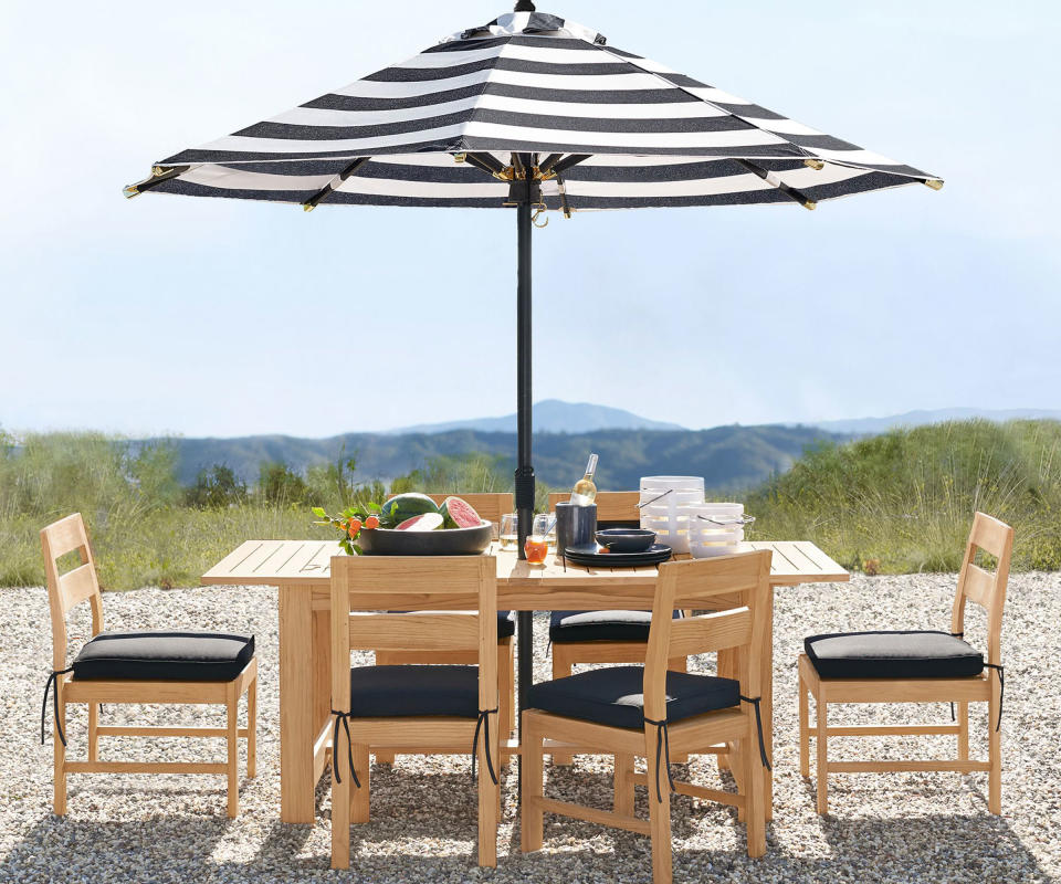 teak outdoor dining table and chairs with a black and white striped patio umbrella on a patio