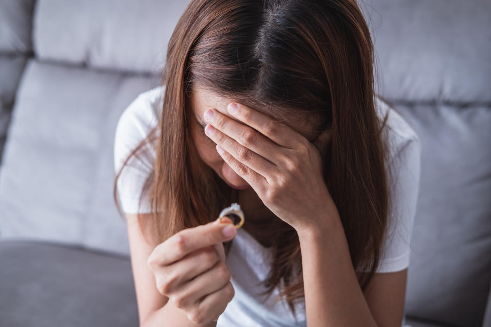 A woman holding a wedding ring and covering her face with her hand