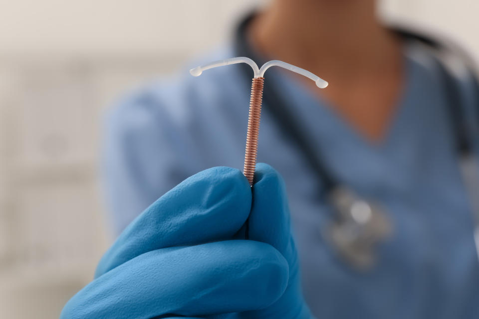 A person wearing blue medical gloves holds up an intrauterine device (IUD) in a healthcare setting