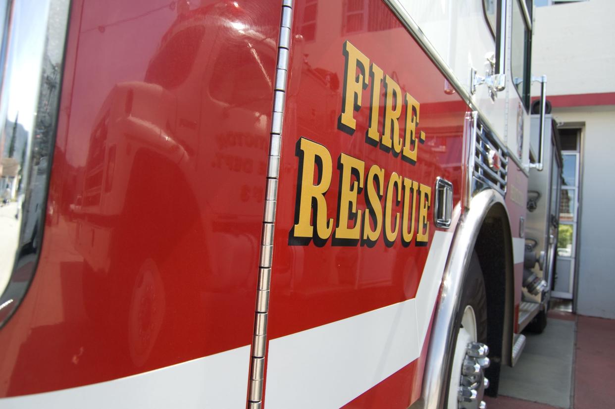 A view down the length of a fire truck parked in front of a fire station, with fire rescue labeled on the side.