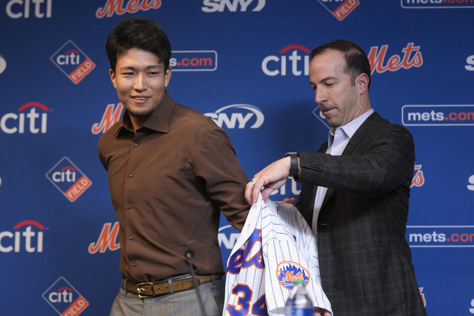 New York Mets Kodai Senga, left, puts on his new jersey with the help of general manager Billy Eppler during a news conference at Citi Field, Monday, Dec. 19, 2022, in New York. The Japanese pitcher and the New York Mets baseball team have finalized a $75 million, five-year contract. (AP Photo/Seth Wenig)