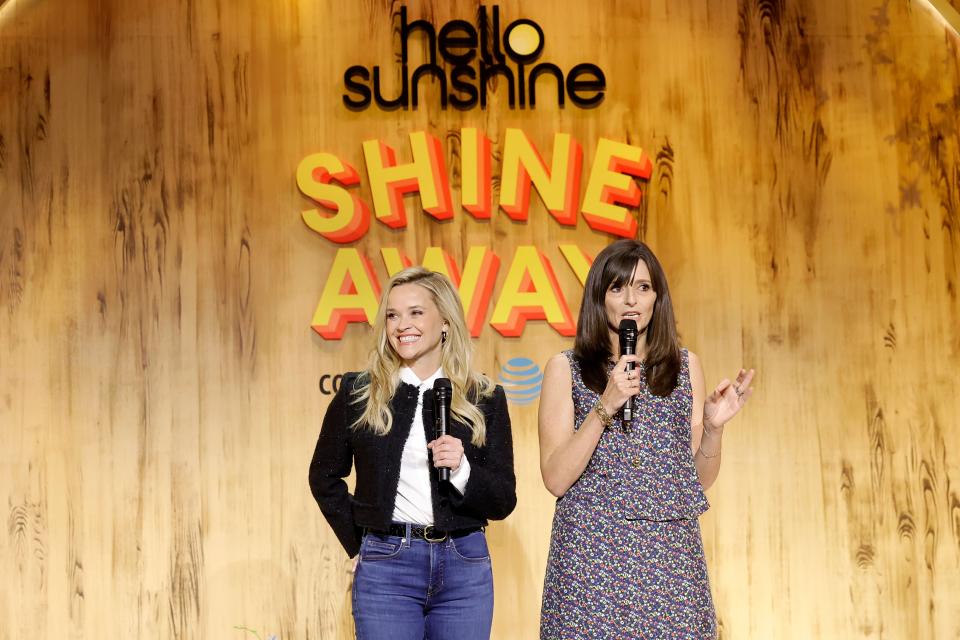 Reese Witherspoon and Sarah Harden speak at the Hello Sunshine Shine Away event, standing on stage holding microphones