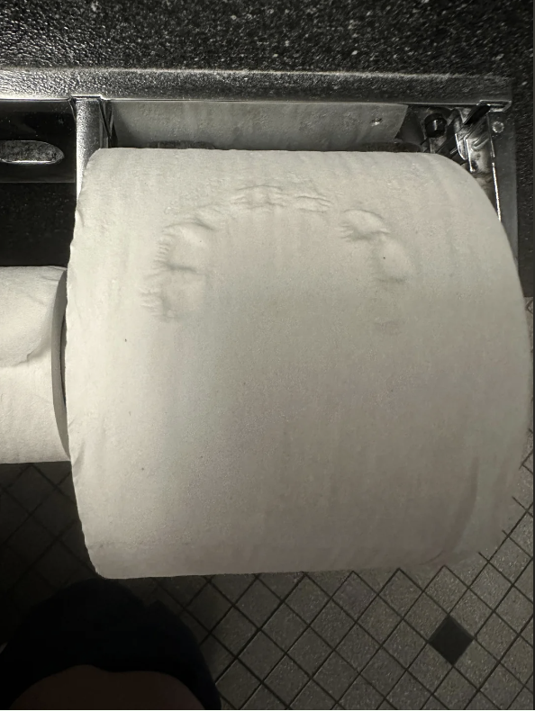 Close-up of a roll of toilet paper with an imprint of a face, found in a restroom