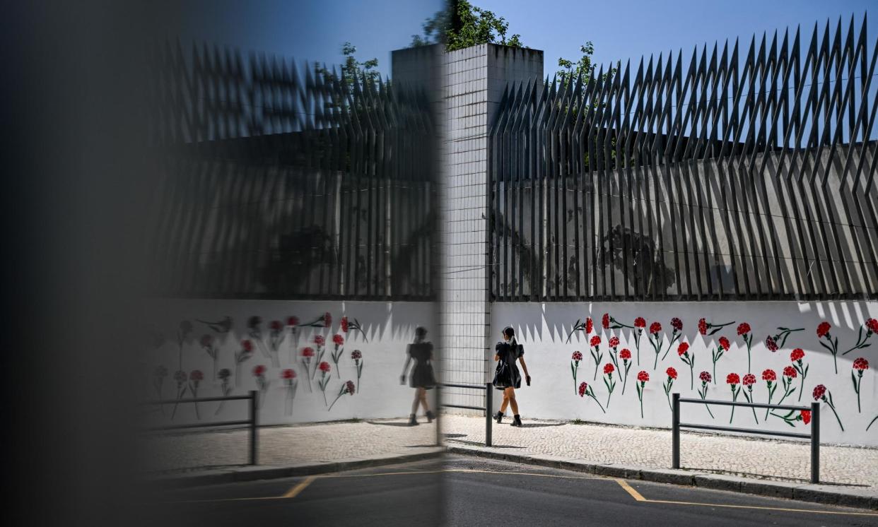 <span>A woman walks past the Lisbon University of Social and Human Sciences walls, stenciled with red carnations, in Lisbon. </span><span>Photograph: Patrícia de Melo Moreira/AFP/Getty Images</span>