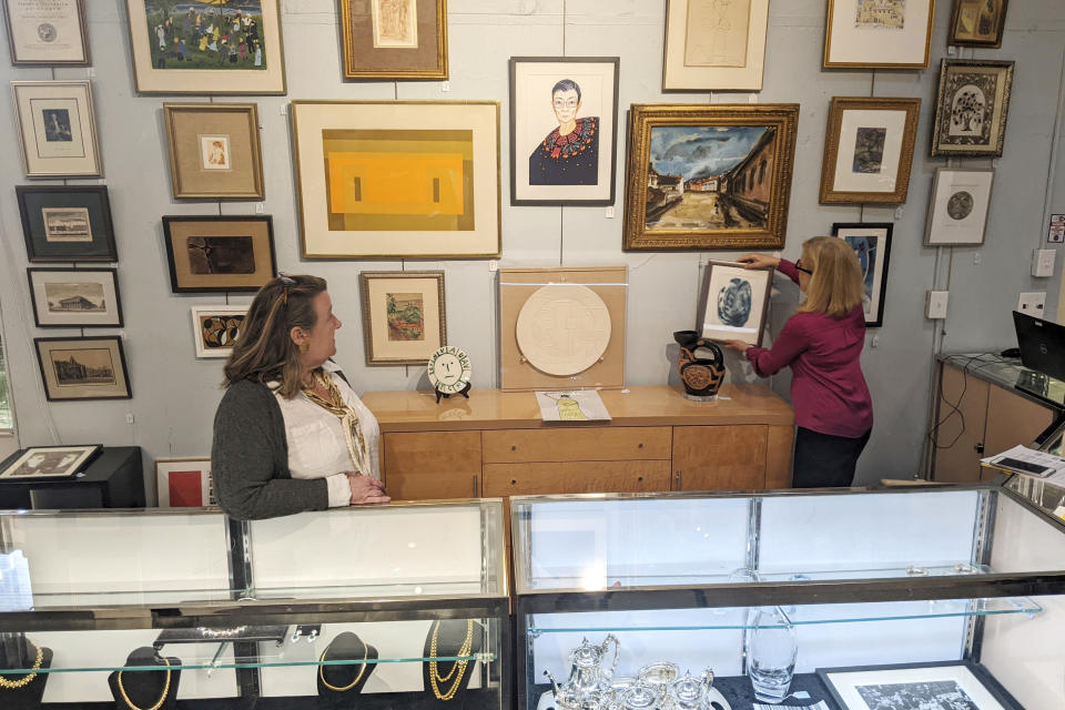 FILE - In this image from video, Elizabeth Haynie Wainstein, right, hangs up a piece of modern art belonging to the late Justice Ruth Bader Ginsburg inside Potomack Company Auctions in Alexandria, Va., Monday, April 11, 2022. An online auction of 150 of items owned by Ginsburg raised $803,650 for Washington National Opera. The opera was one of the late justice’s passions. (AP Photos/Nathan Ellgren, File)