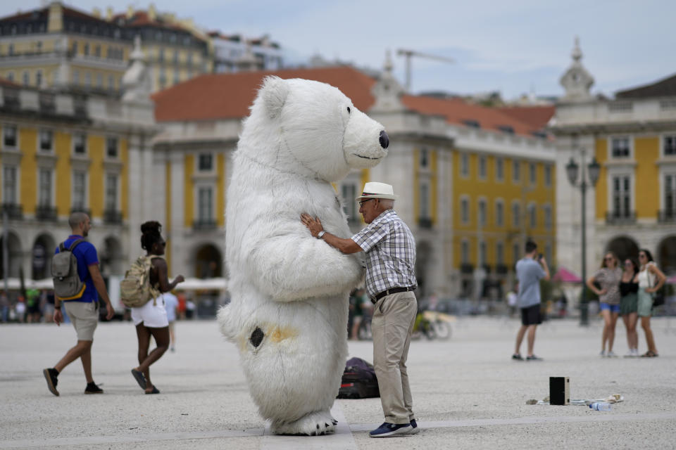 A man talks to a person wearing a polar bear costume at Lisbon's Comercio square, Monday, July 11, 2022. Temperatures in Portugal have dropped in the last couple days bringing some respite from a heatwave but are expected to rise again Tuesday and reach 46 degrees Celsius (115 Fahrenheit) in some parts of the country by Thursday. (AP Photo/Armando Franca)