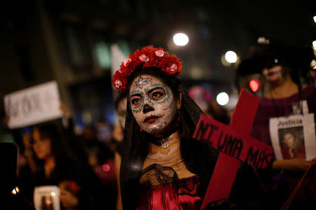 An activist with her face painted to look like the popular Mexican figure "Catrina" holds a cross as she takes part in a march against femicide during the Day of the Dead in Mexico City, Mexico, November 1, 2017. The word on the cross read: "No one more". REUTERS/Carlos Jasso