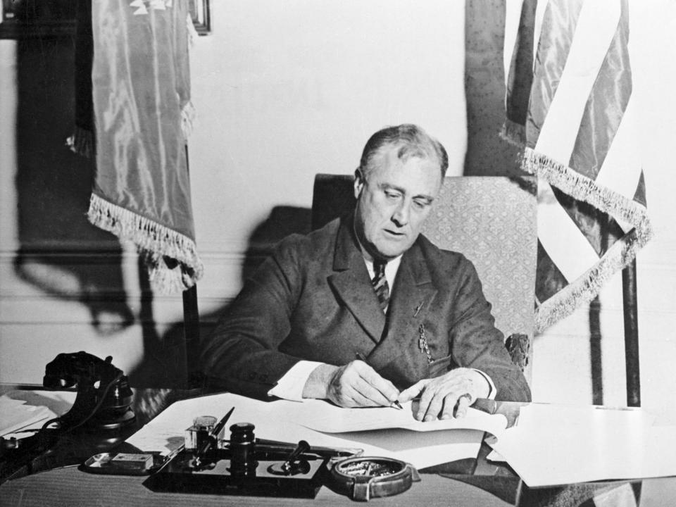 Franklin Delano Roosevelt signing papers at his desk.
