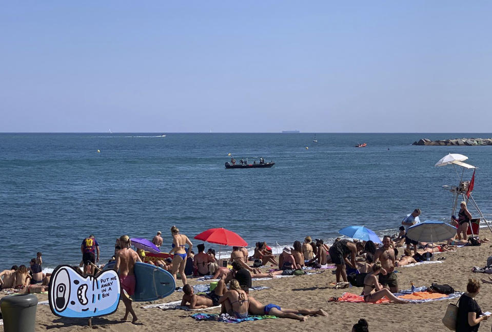 A police boat works after locating possible explosive device in the sea while people sunbathe on an open part of a beach in Barcelona, Spain, Sunday Aug. 25, 2019. Authorities in Barcelona have evacuated one of the Spanish city's popular beaches after reports of a possible explosive device there, though reports indicated it was an old, possibly wartime device and was underwater off the coast. (AP Photo/Ignacio Murillo)