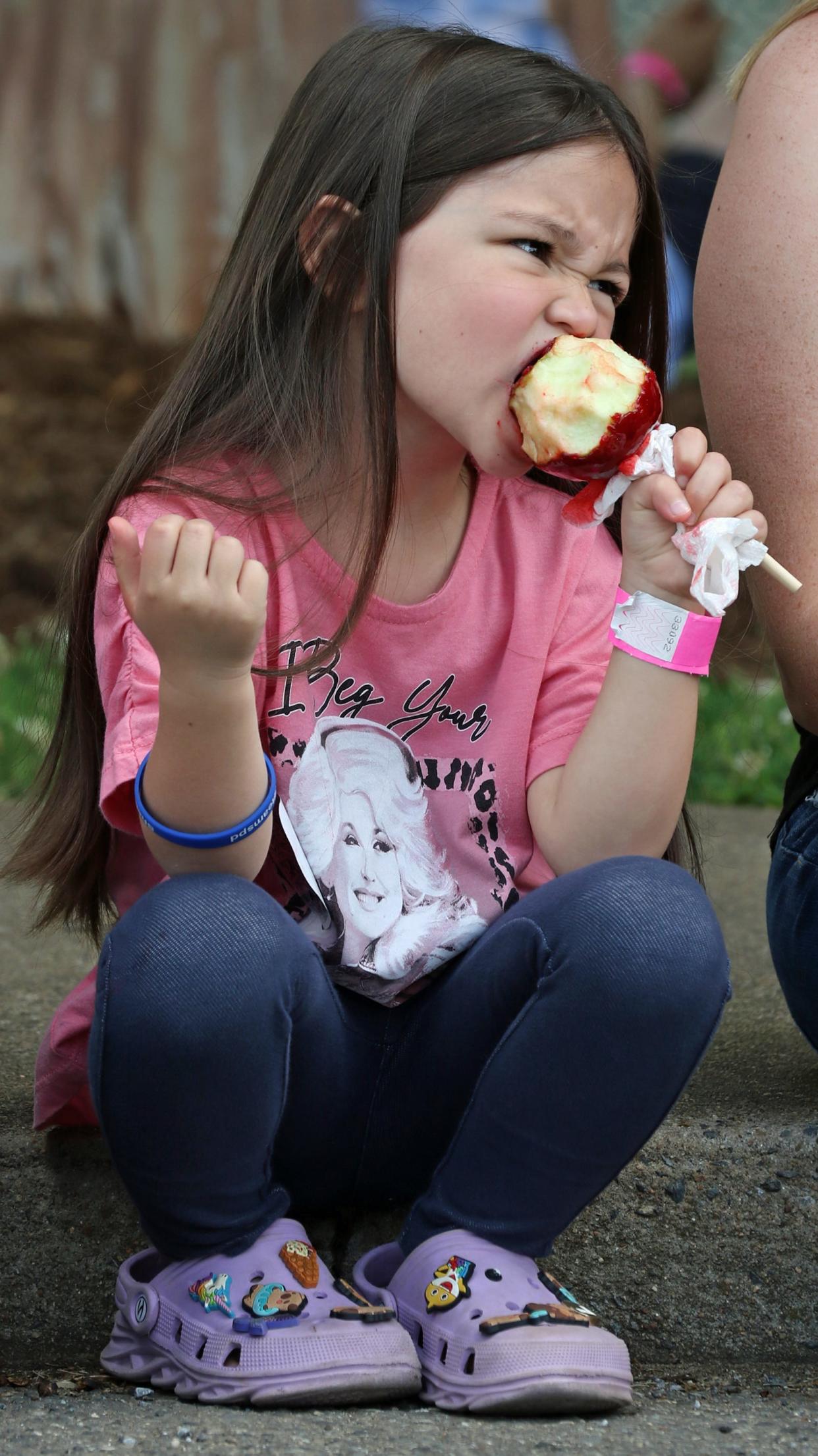 Five-year-old Lela Dalton bites into a candy apple during the 2024 Foothill's Merry-Go-Round Festival held Saturday, April 27, 2024, at the Shelby City Park.