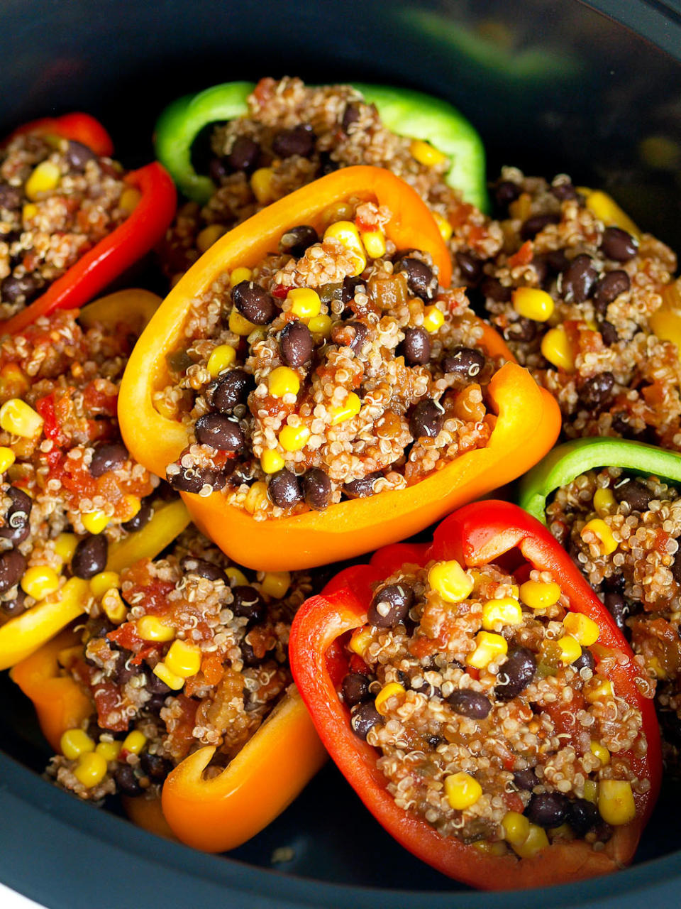 a bowl of peppers sliced in half and filled with quinoa, corn, and beans