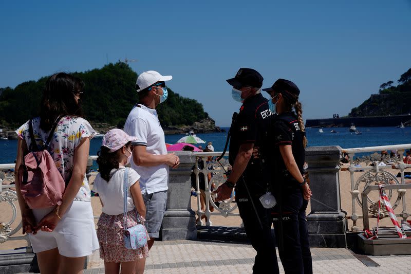Una familia con mascarillas habla con la policía en la playa de Ondarreta en San Sebastián