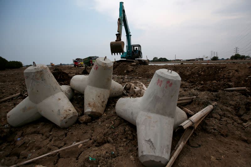 A worker operates an excavator at a construction site, building a wave breaker, near Tambakrejo, a village affected by rising sea level and land subsidence in Semarang