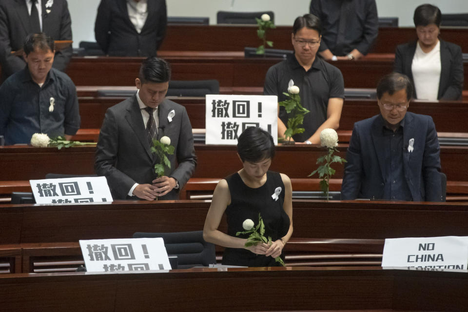 Pro-democracy lawmakers pay a silent tribute to the man who fell to his death on Saturday evening after hanging a protest banner on scaffolding on a shopping mall, at the Legislative Council in Hong Kong, Wednesday, June 19, 2019. Hong Kong lawmakers are meeting for the first time in a week, after massive protests over an extradition bill that eventually was suspended. The placards with Chinese read "Withdraw". (AP Photo/Kin Cheung)