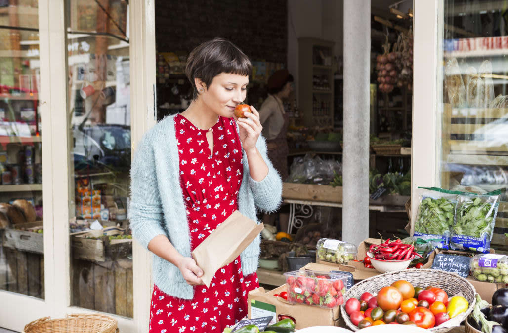 Woman smelling fresh tomato at organic farm shop.