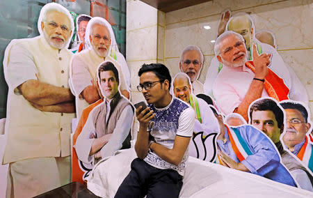 A worker talks on a mobile phone as he sits next to the cutouts of Indian politicians at a shop selling election campaign materials in the old quarters of Delhi, India, April 8, 2019. REUTERS/Anushree Fadnavis