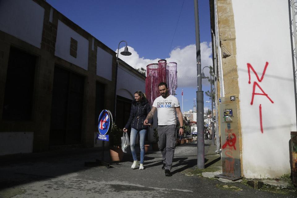 A man and a woman cross the Ledras street checkpoint from the Turkish Cypriot breakaway northern part to the Greek Cypriot area at the south, in the divided capital Nicosia in the eastern Mediterranean island of Cyprus, Wednesday, Jan. 11, 2017. The rivals leaders of Cyprus have begun a third day of talks aimed at reunifying the island split along ethnic Greek and Turkish lines. Graffiti on the wall reads in Greek "YES", referring to the reunification, (AP Photo/Petros Karadjias)