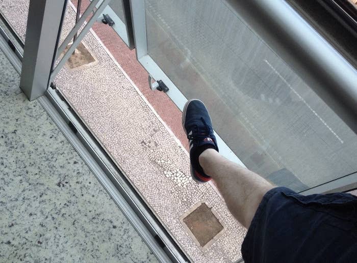Person's leg extended stepping onto a balcony with a clear floor, overlooking lower floors