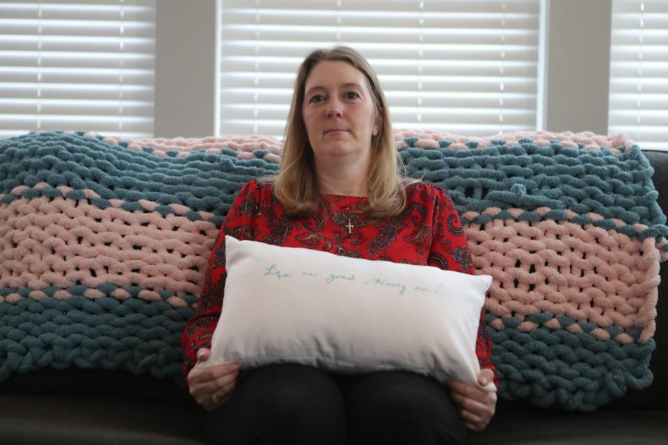 Candace Esham in her Delaware home. She is holding a pillow she made following her grandmother's death. It features the words "Life is good -- hang on!" Esham's grandmother wrote this months before she died.