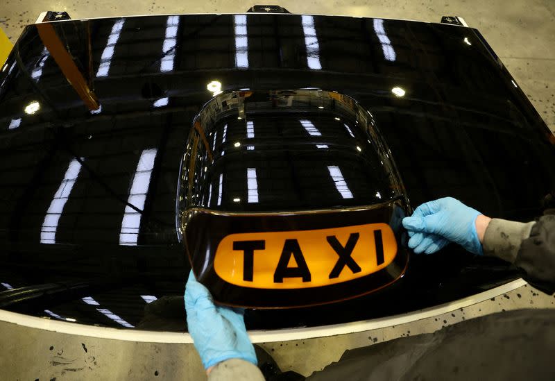 FILE PHOTO: A worker places a taxi sign onto the roof panel of a TX electric taxi inside the LEVC (London Electric Vehicle Company) factory in Coventry