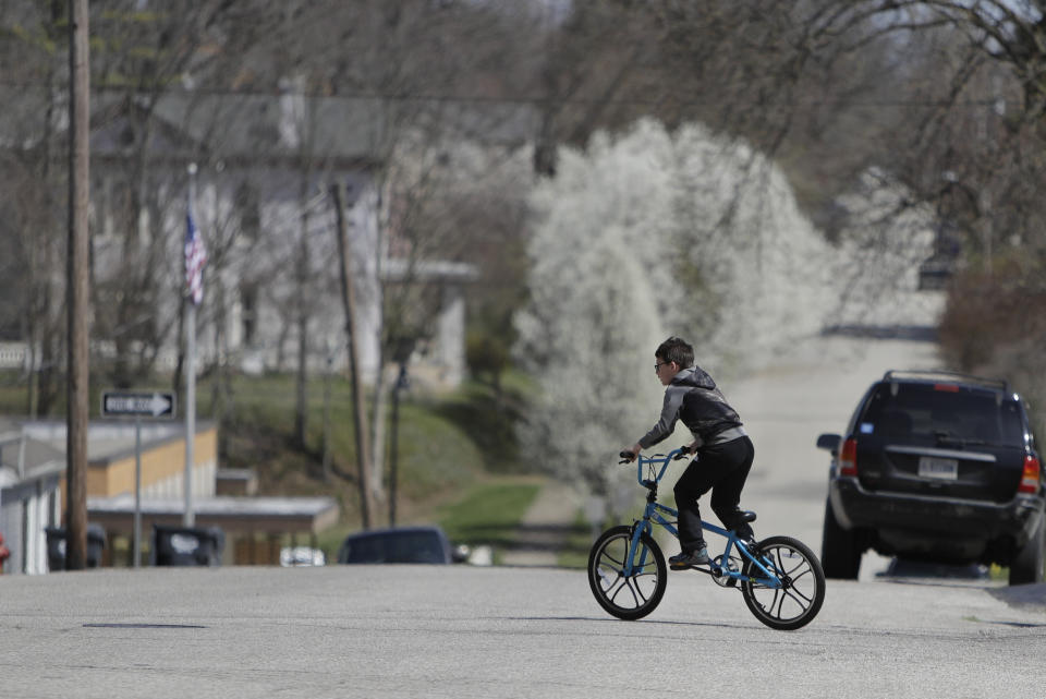 A bike rider crosses the street on his bike, Thursday, April 2, 2020, in Greensburg, Ind. Decatur County is among three neighboring southeastern Indiana counties that all have confirmed COVID-19 cases among the highest per-capita rates in the country. (AP Photo/Darron Cummings)