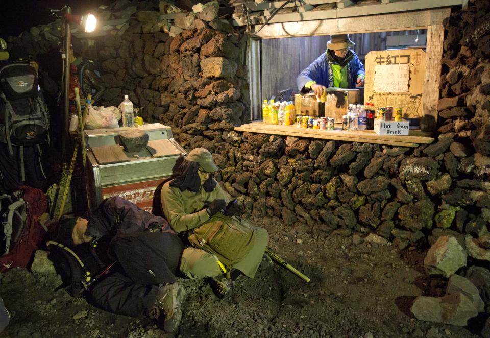 In this Sunday, Aug. 11, 2013 photo, hikers rest next to a snack stand on the summit of Mount Fuji in Japan. The Japanese cheered the recent recognition of Mount Fuji as a UNESCO World heritage site, though many worry that the status may worsen the damage to the environment from the tens of thousands who visit the peak each year. (AP Photo/David Guttenfelder)