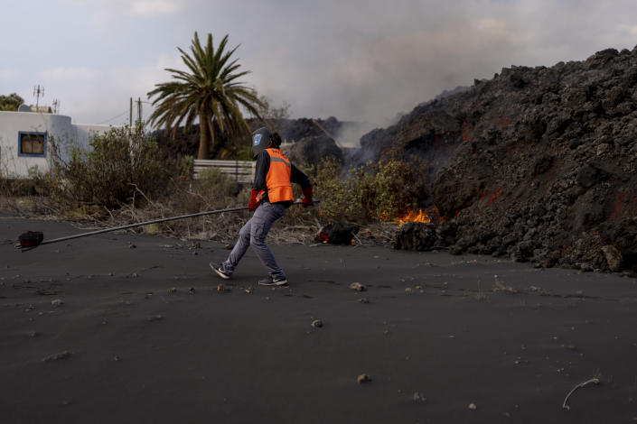 A scientist with the Canary Islands' volcanology institute, Involcan, carries a rock of lava during field work in the surroundings of the volcano on the Canary island of La Palma, Spain, Saturday, Oct. 30, 2021. Scientists from around the world flocking to an eastern Atlantic Ocean island are using an array of new technologies available to them in 2021 to scrutinize — from land, sea, air, and even space — a rare volcanic eruption. But despite technological and scientific leaps, predicting volcanic eruptions and, more crucially, how they end, remains a mystery. (AP Photo/Emilio Morenatti)