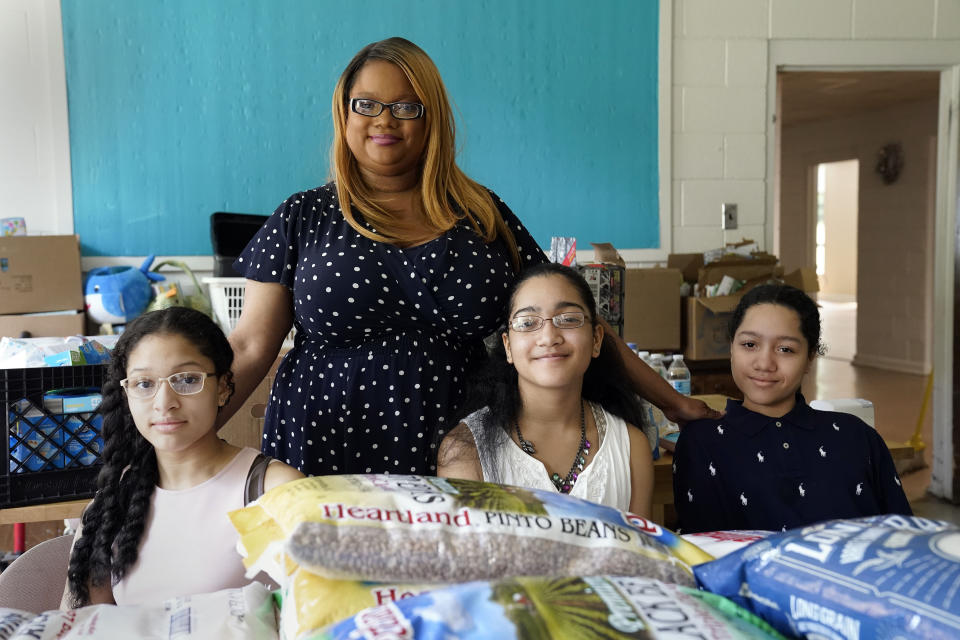 Aja Purnell-Mitchell stands next to her three children, Kyla, 13, left; Kyra, 15, and Cartier, 14, at a local food hub in Durham, N.C., on Friday, May 28, 2021, where they often help their mother. The teenagers have been learning remotely since last March but now plan to attend summer school after being vaccinated. (AP Photo/Gerry Broome)