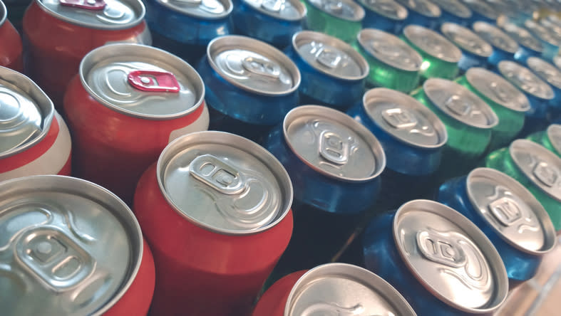 Rows of unopened soda cans of various brands arranged closely together, showcasing their tops and pull tabs